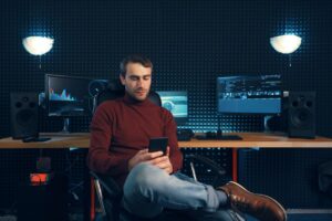 Young man working in the studio using a smartphone and computer.